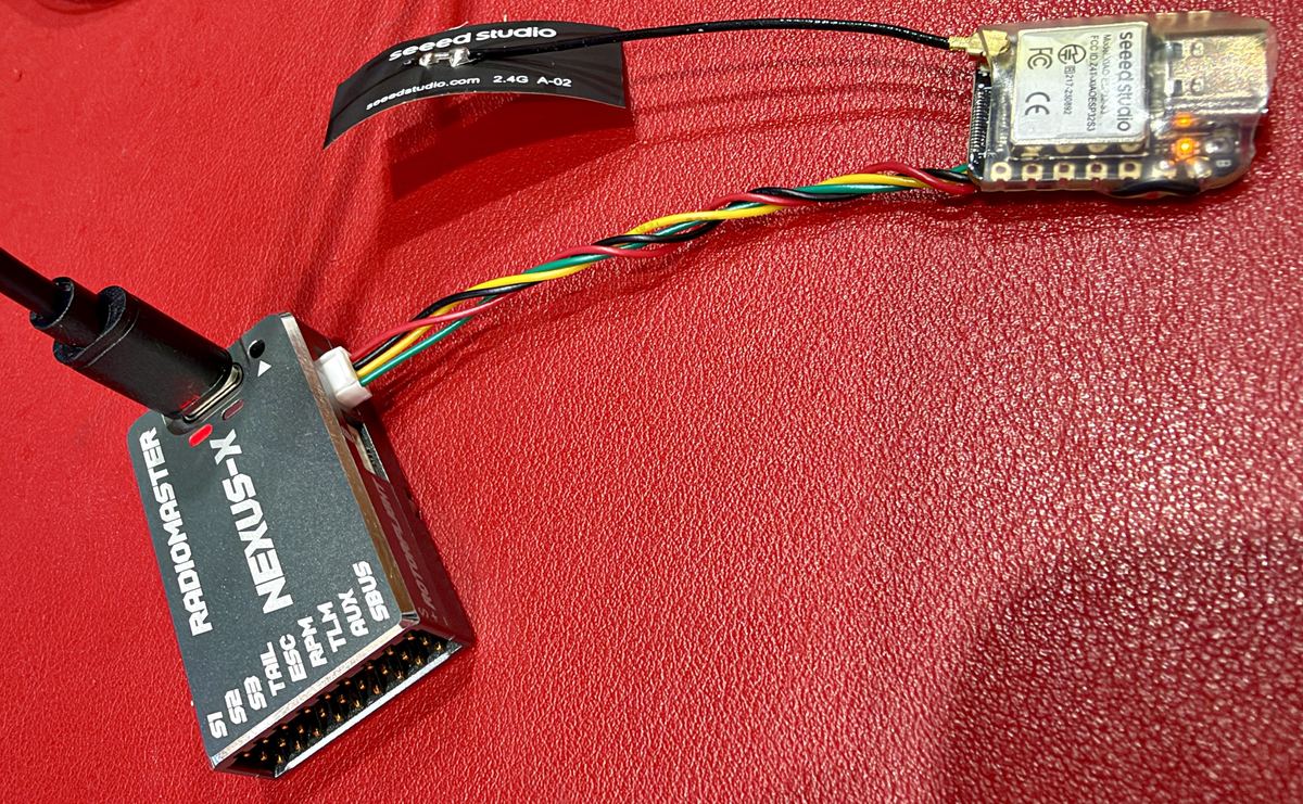 The dongle: a bare XIAO ESP32-S3 with its antenna, wired by a four-wire lead to a RadioMaster Nexus-X, with the USB-C cable in the Nexus